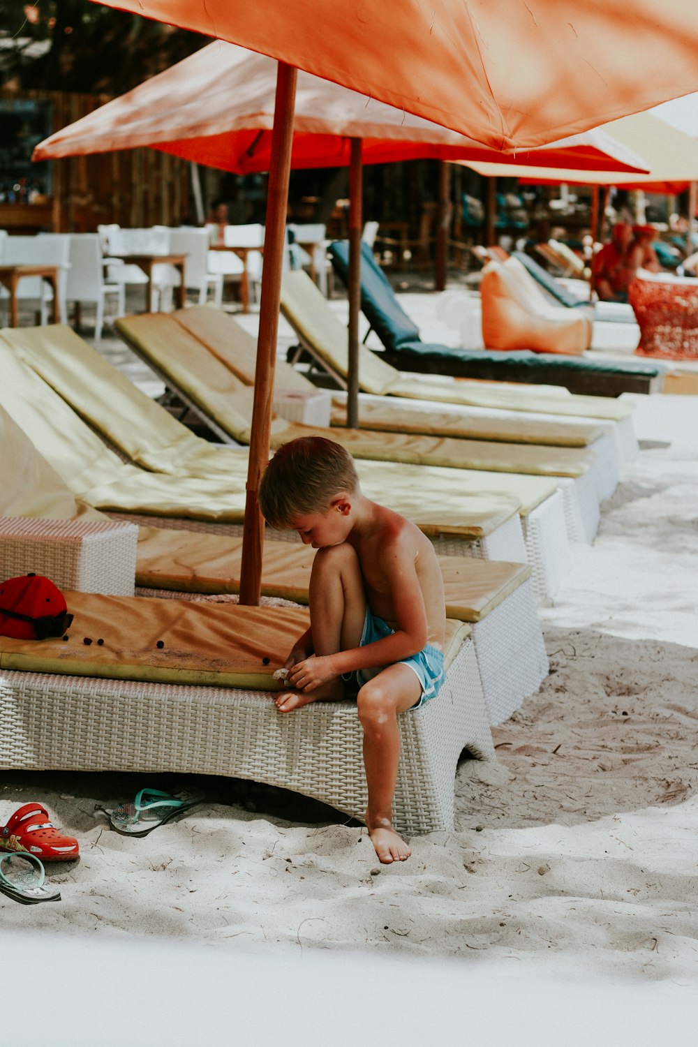 boy sitting on white wicker chaise lounge on beach