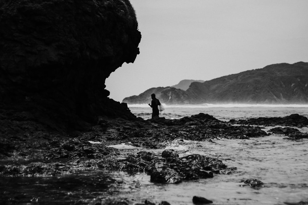 grayscale photo of person under cliff