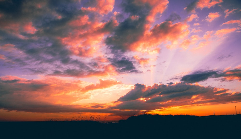 silhouette of hills under orange and gray sky at golden hour