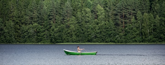 woman in blue shirt riding on green boat on river during daytime in Sulkava Finland