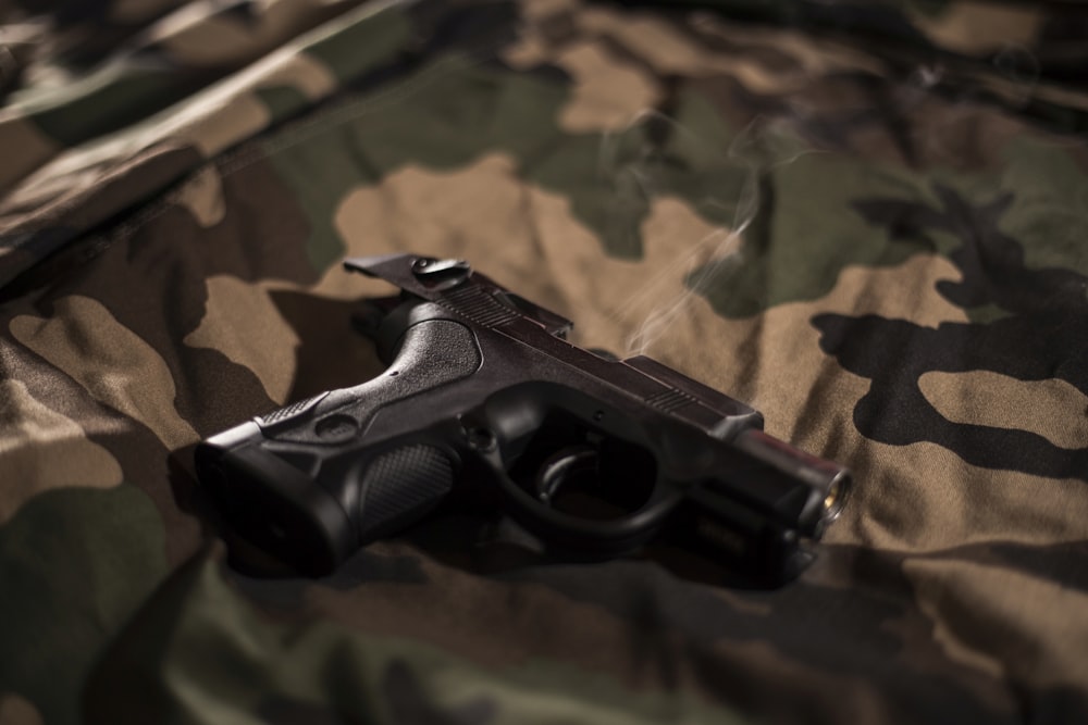 Pistola negra sobre hoja de camuflaje verde, marrón y negro