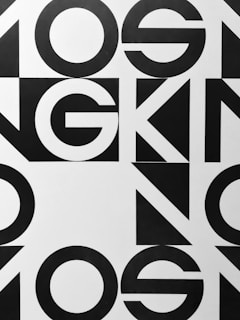 Bold black and white geometric typography with large, overlapping letters and shapes, creating an abstract pattern.