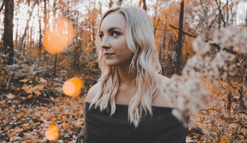 woman wearing black off-shoulder shirt taking pose near trees during daytime