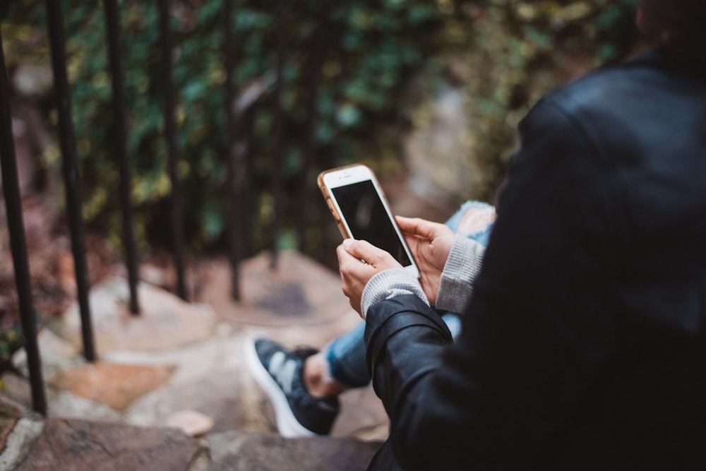 Persona sosteniendo un teléfono inteligente blanco sentado en la escalera