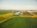An aerial view of expansive agricultural fields stretching across the landscape, with a river winding through the center. The fields are divided into various sections with different shades of green and brown, indicating diverse crops or stages of growth.