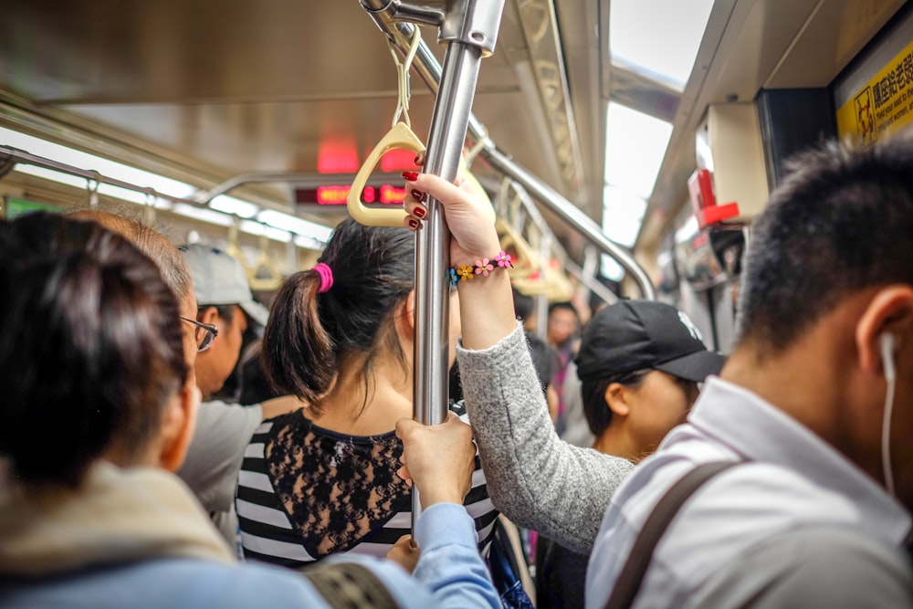 personas sosteniendo un poste de metal mientras están de pie dentro del tren