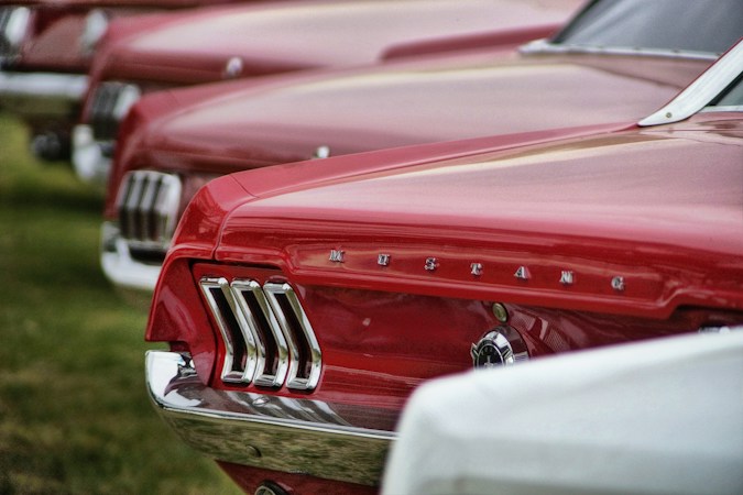A row of restored red Ford Mustangs lined up at a community car show