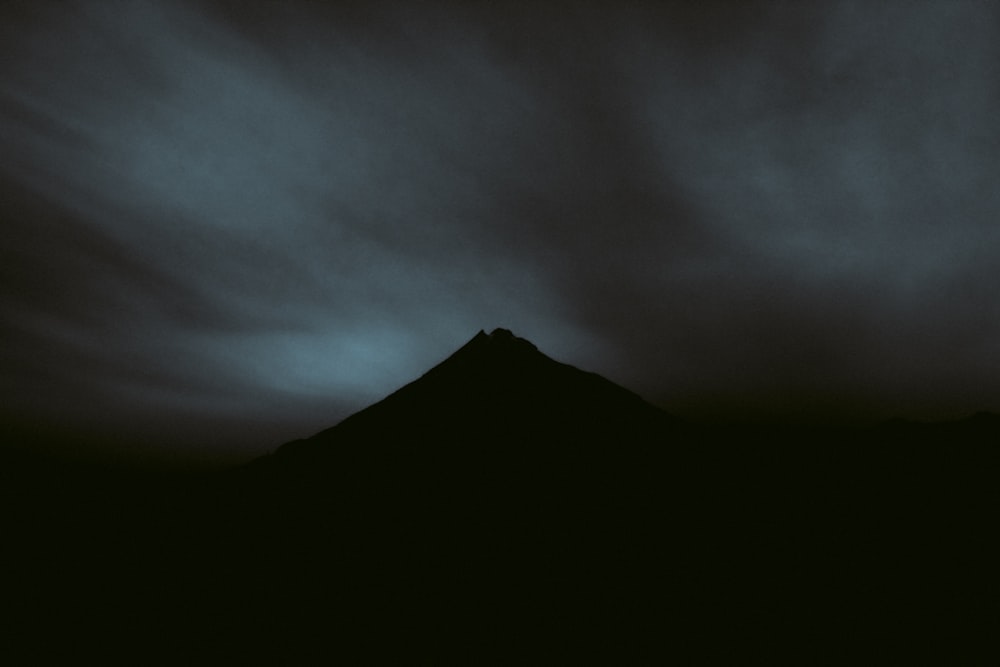 a black and white photo of a mountain under a cloudy sky