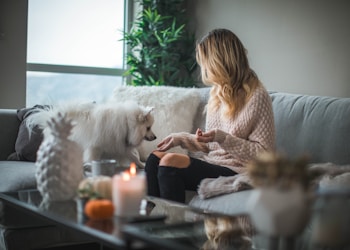 woman sitting on sofa while holding food for dog