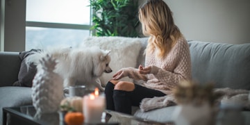 woman sitting on sofa while holding food for dog