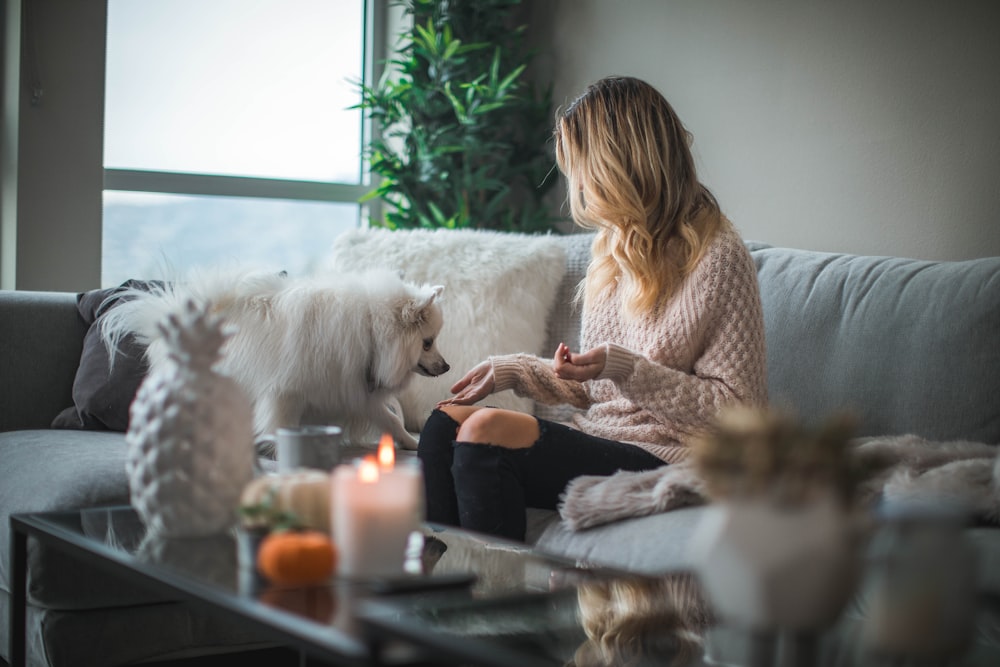 Frau sitzt auf dem Sofa, während sie Futter für Hund hält