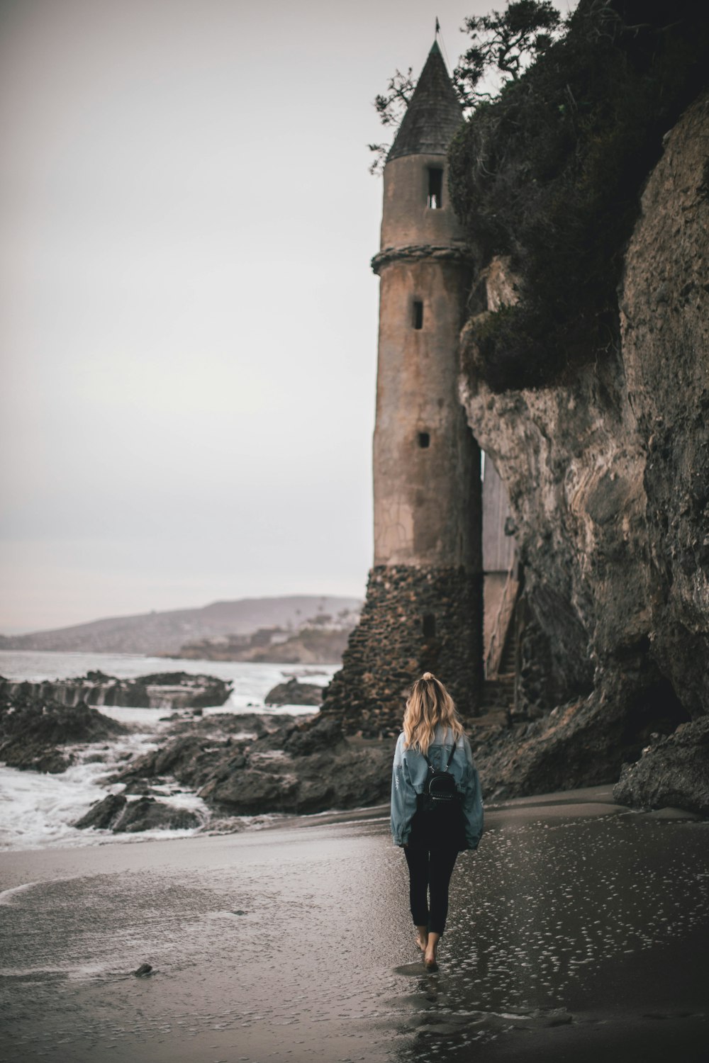茶色の灯台の近くの海岸に立つリュックサックを背負った女性