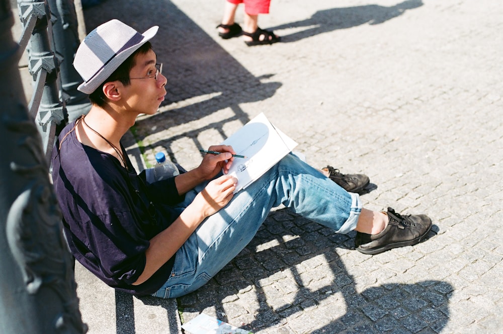 man leaning on metal rail holding pen and notebook outside