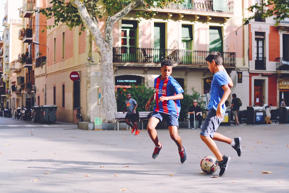 dois meninos jogando futebol perto do prédio durante o dia