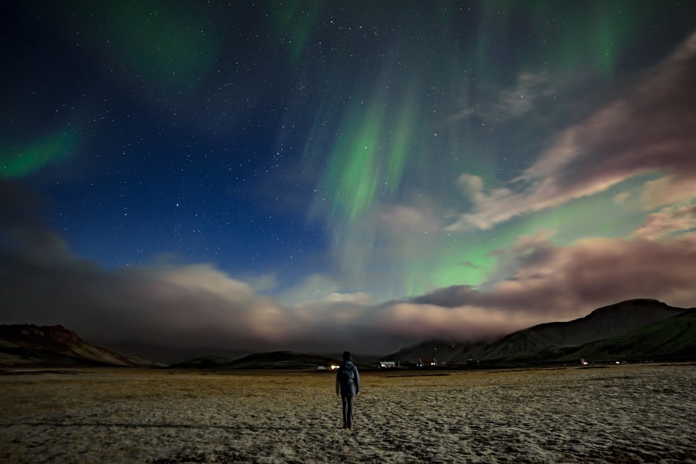 man standing near mountain under Aurora Borealis