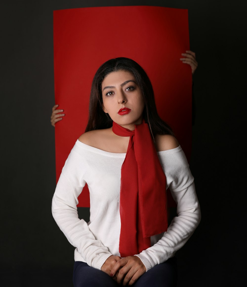 赤い板紙の前に白い長袖のトップスと赤いスカーフの女性