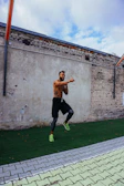 Dynamic shot of a man wearing workout gear mid-jump against a graffiti wall.