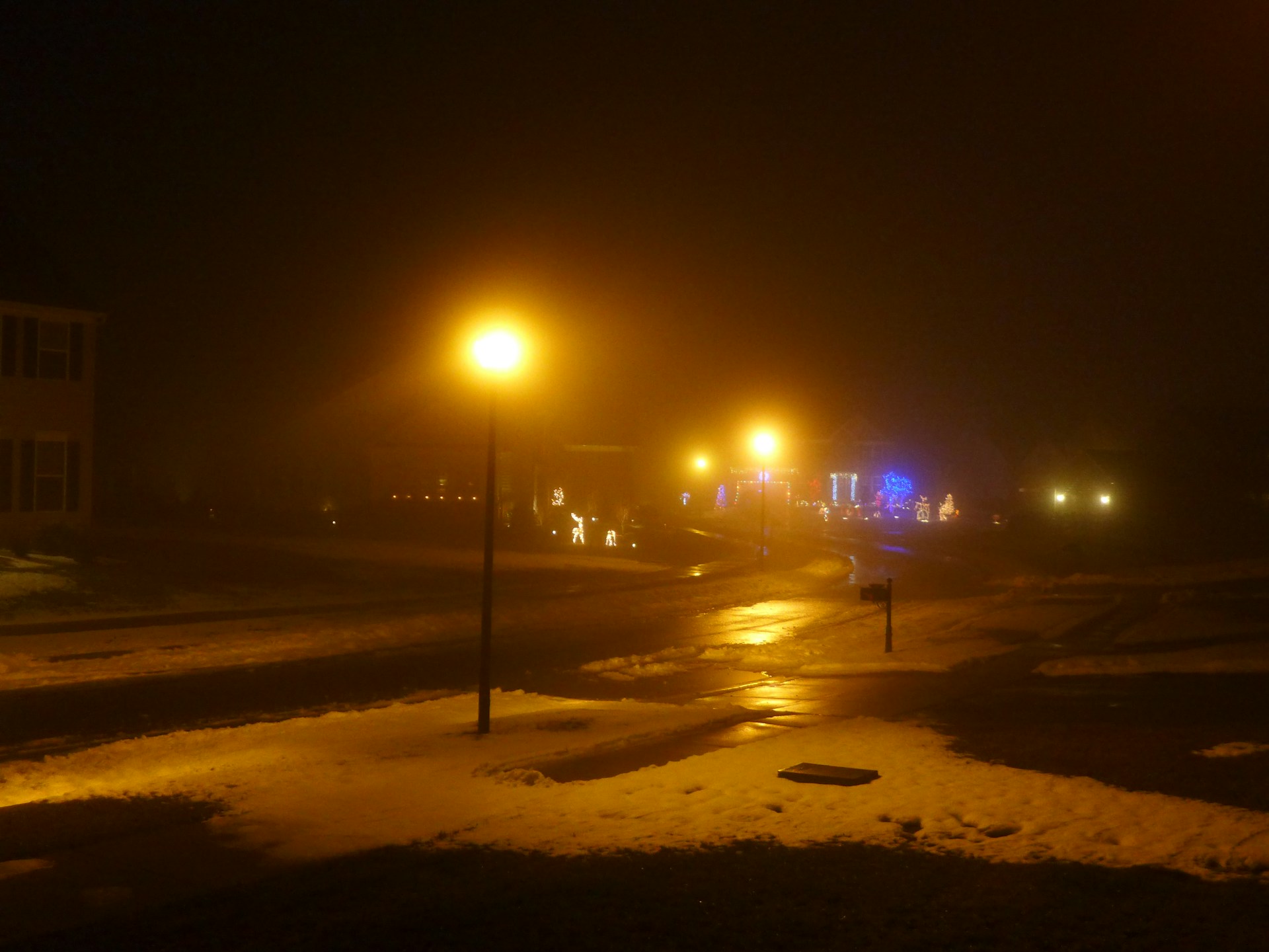 A cozy street scene in Moralzarzal at night, with snow gently falling and holiday decorations glowing.