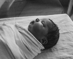 grayscale photography of sleeping baby covered by textile