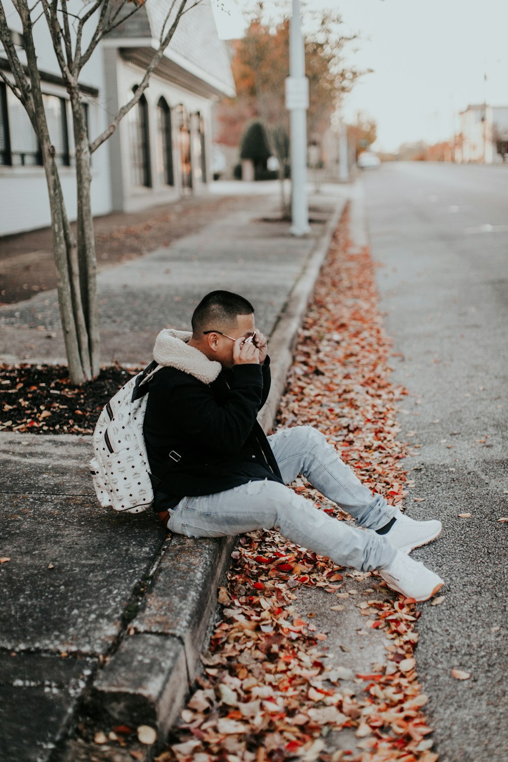 man sitting beside empty road during daytime