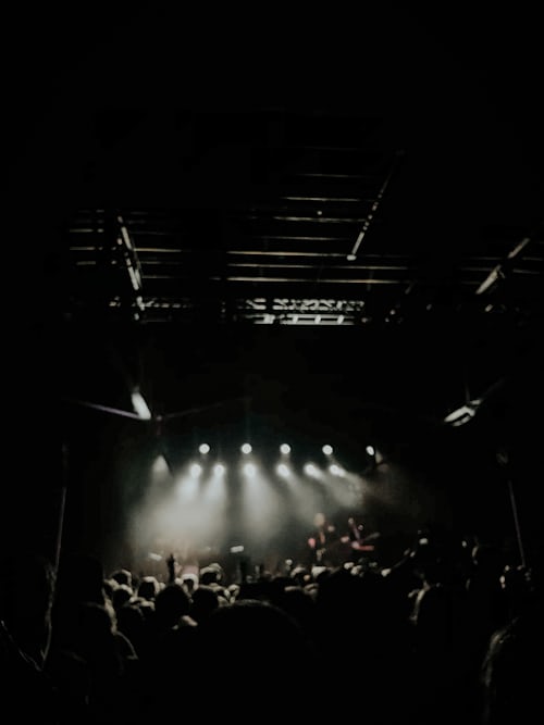 dark room, lit stage, crowd looking on some with hands raised