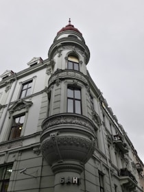 A historic building with ornate architectural details, including an intricately designed turret topped with a red dome. The facade features detailed stucco work and large windows. The word 'банк' is displayed near the entrance, indicating it is a bank.