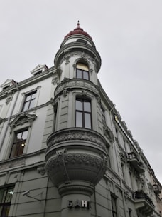 A historic building with ornate architectural details, including an intricately designed turret topped with a red dome. The facade features detailed stucco work and large windows. The word 'банк' is displayed near the entrance, indicating it is a bank.