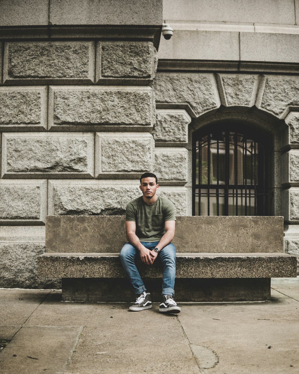 homem sentado em banco de concreto fora do prédio