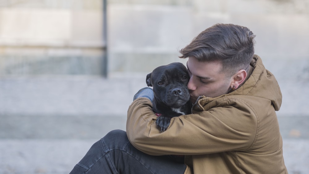 Fotografia a fuoco selettiva dell'uomo che abbraccia il cane nero