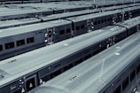 Several train cars are arranged in neat parallel rows in a train yard. The metallic surfaces of the trains create a uniform, industrial appearance. The trains are parked closely together, highlighting the scale and efficiency of the organization.