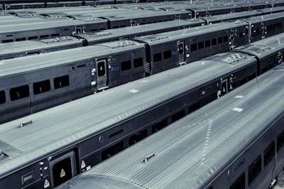 Several train cars are arranged in neat parallel rows in a train yard. The metallic surfaces of the trains create a uniform, industrial appearance. The trains are parked closely together, highlighting the scale and efficiency of the organization.