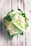A fresh head of cauliflower with green leaves partially covering the white, bumpy florets. The cauliflower rests on a rustic, whitewashed wooden surface with some visible water droplets, suggesting freshness.