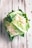A fresh head of cauliflower with green leaves partially covering the white, bumpy florets. The cauliflower rests on a rustic, whitewashed wooden surface with some visible water droplets, suggesting freshness.