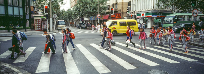 A group of diverse children crossing a street safely, guided by a crossing guard.