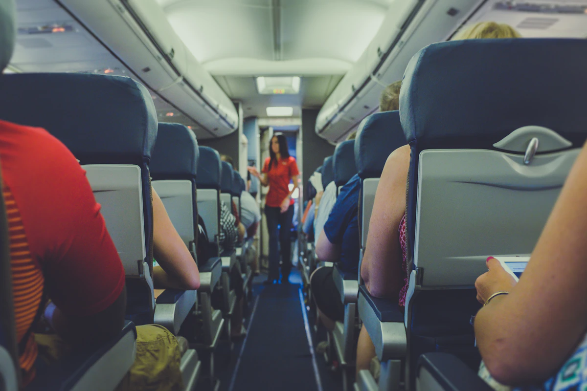 Flight attendant standing in the aisle between passenger seats on an airplane