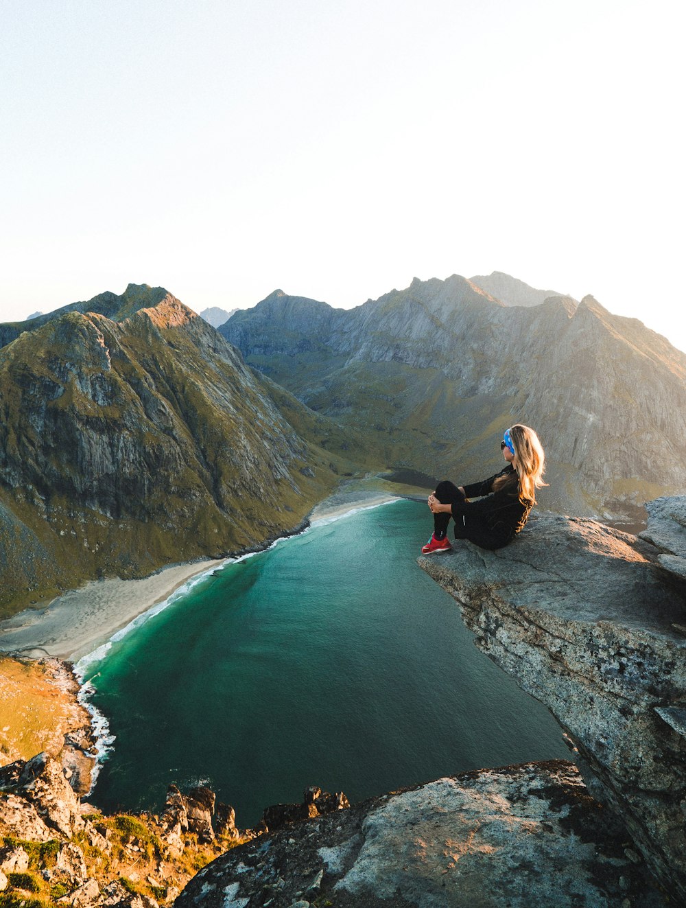 Mujer sentada en el acantilado con vistas al cuerpo de agua cerca de las montañas durante el día