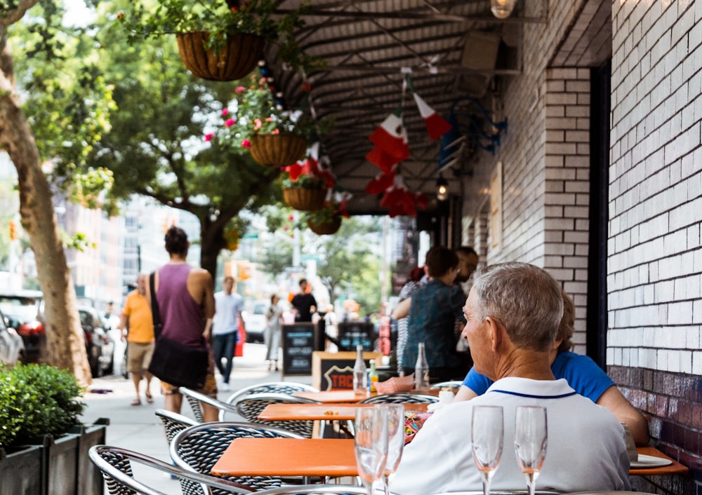 Gente cenando fuera de un restaurante cerca de aparcamientos bajo los árboles