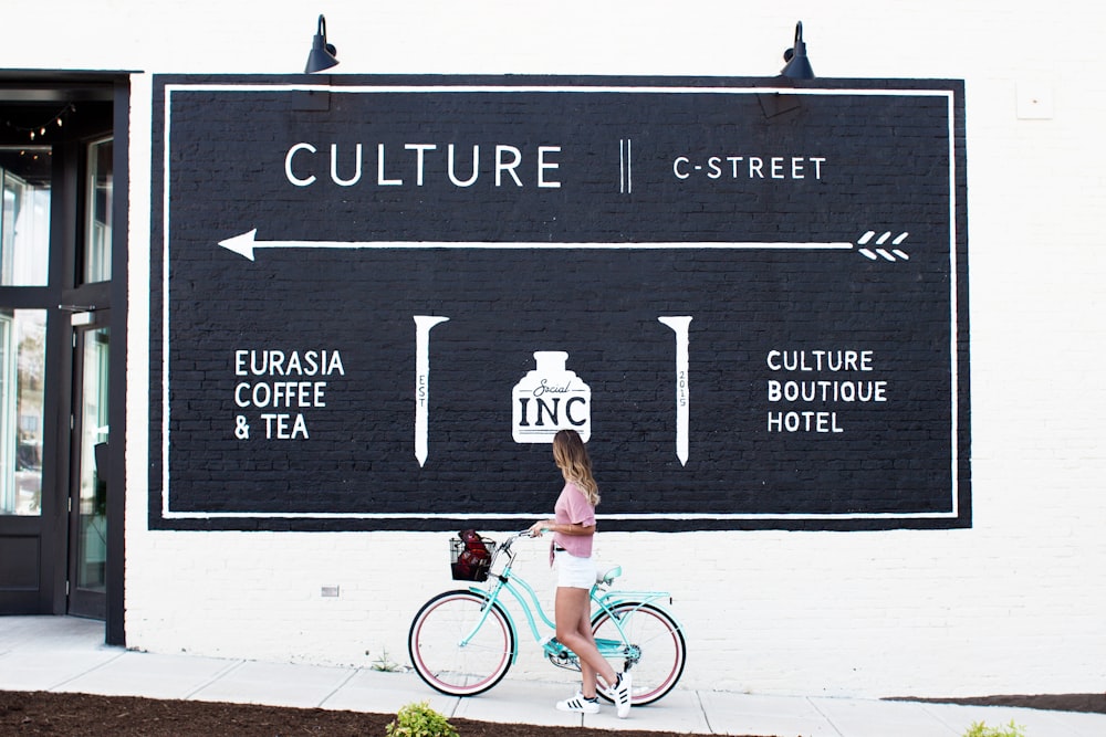 Frau fährt auf blaugrünem Fahrrad und beobachtet Poster auf der Straße