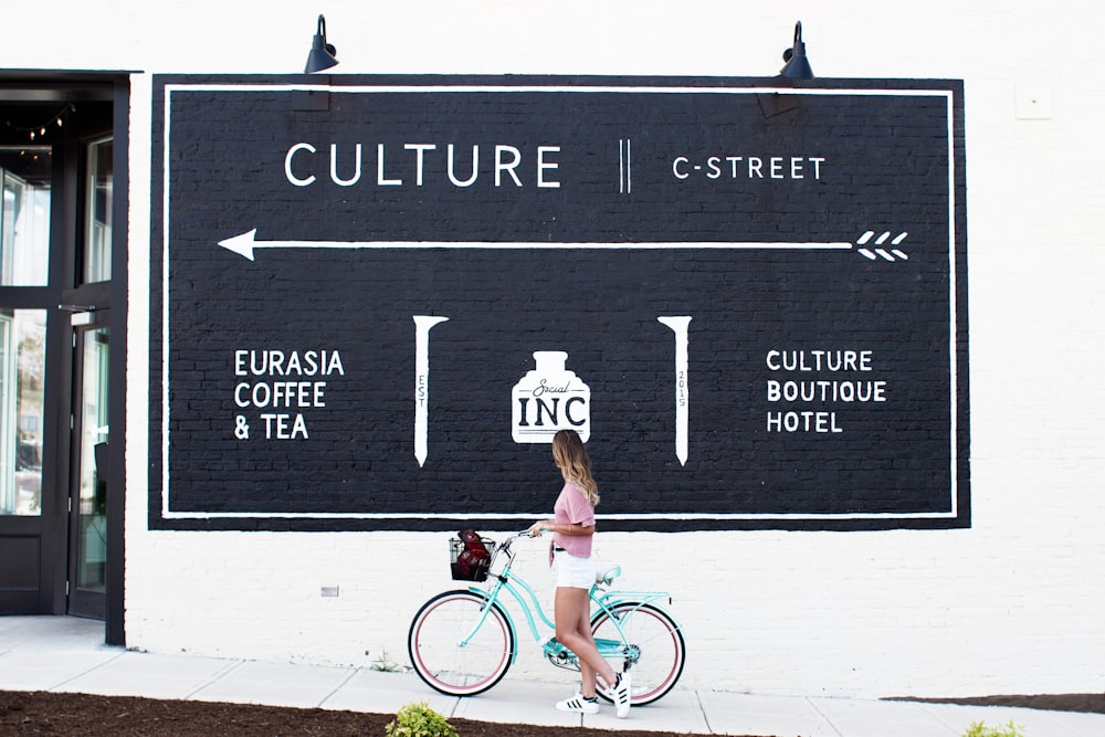 woman ride on teal bike watching poster at the street