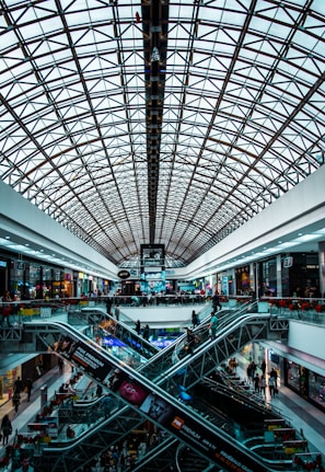 Panoramic glass lift moving inside a bustling shopping mall with shoppers nearby.