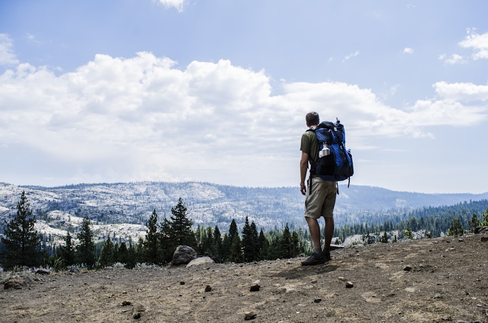 man hiking on brown mountain while carrying blue hiking bag