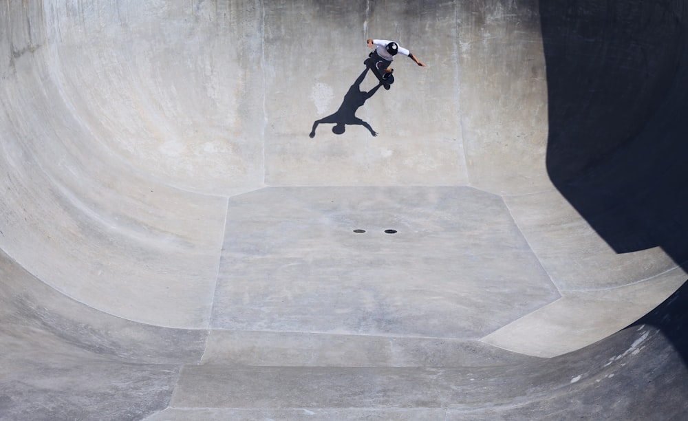 man wearing white t-shirt riding on a skateboard playing on the giant half bowl