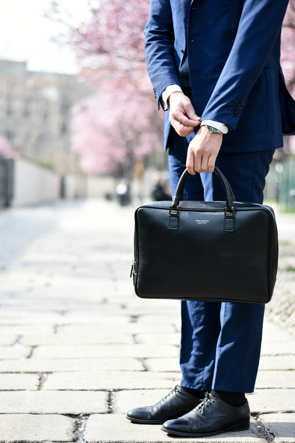 homme en costume bleu debout sur le côté de la rue tout en tenant un sac pendant la journée