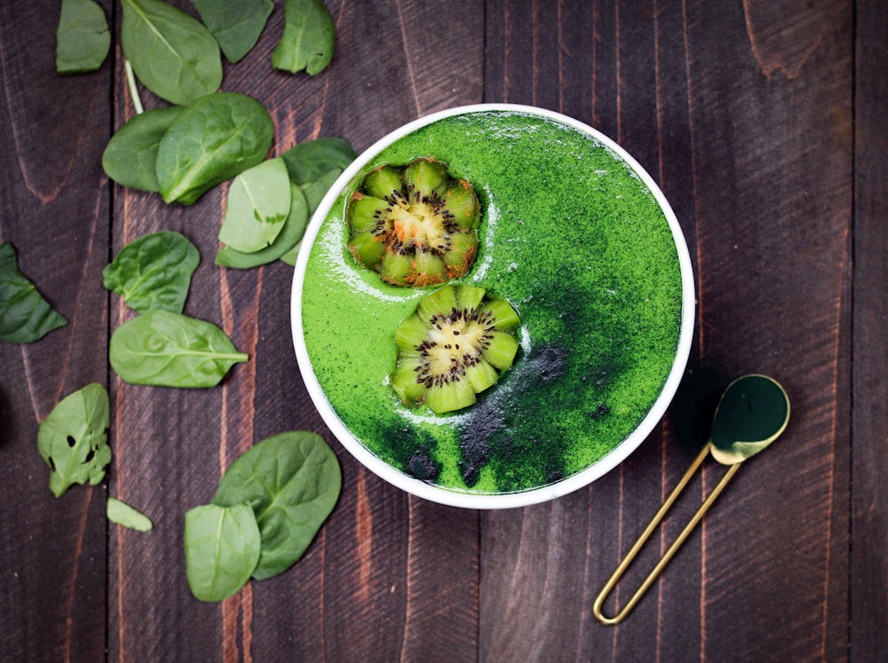 green liquid in white ceramic container with brass-colored spoon on brown wooden surface