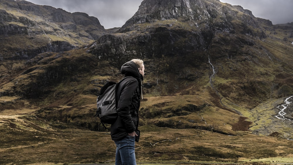 man standing in front mountain under gray sky