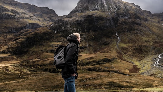 man standing in front mountain under gray sky in Highland United Kingdom