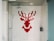 A shower area with white tiles featuring a pixelated red stag design on the back wall. The shower fixtures include a modern square showerhead and a handheld shower wand. The space is enclosed by a glass door and has a minimalist style.