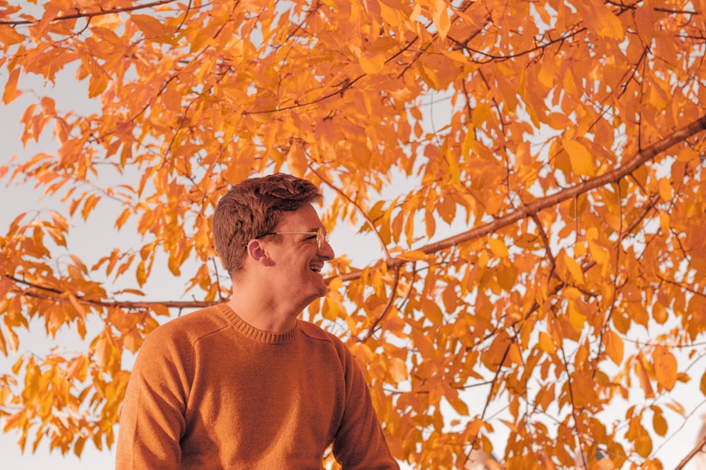 uomo in piedi davanti all'albero di foglie marroni