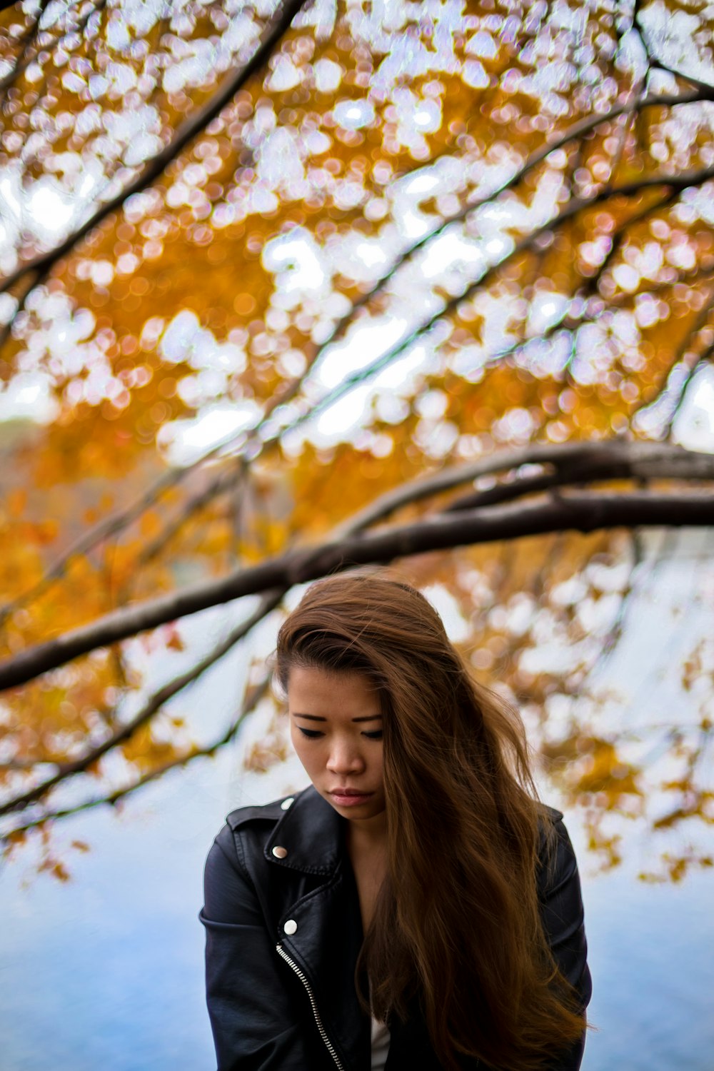 woman wearing black leather jacket under orange leafed tree during daytime