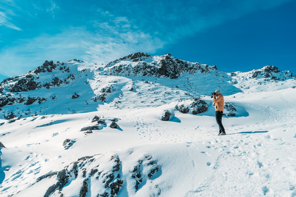 persona che scatta foto in cima alla montagna coperta di neve durante il giorno